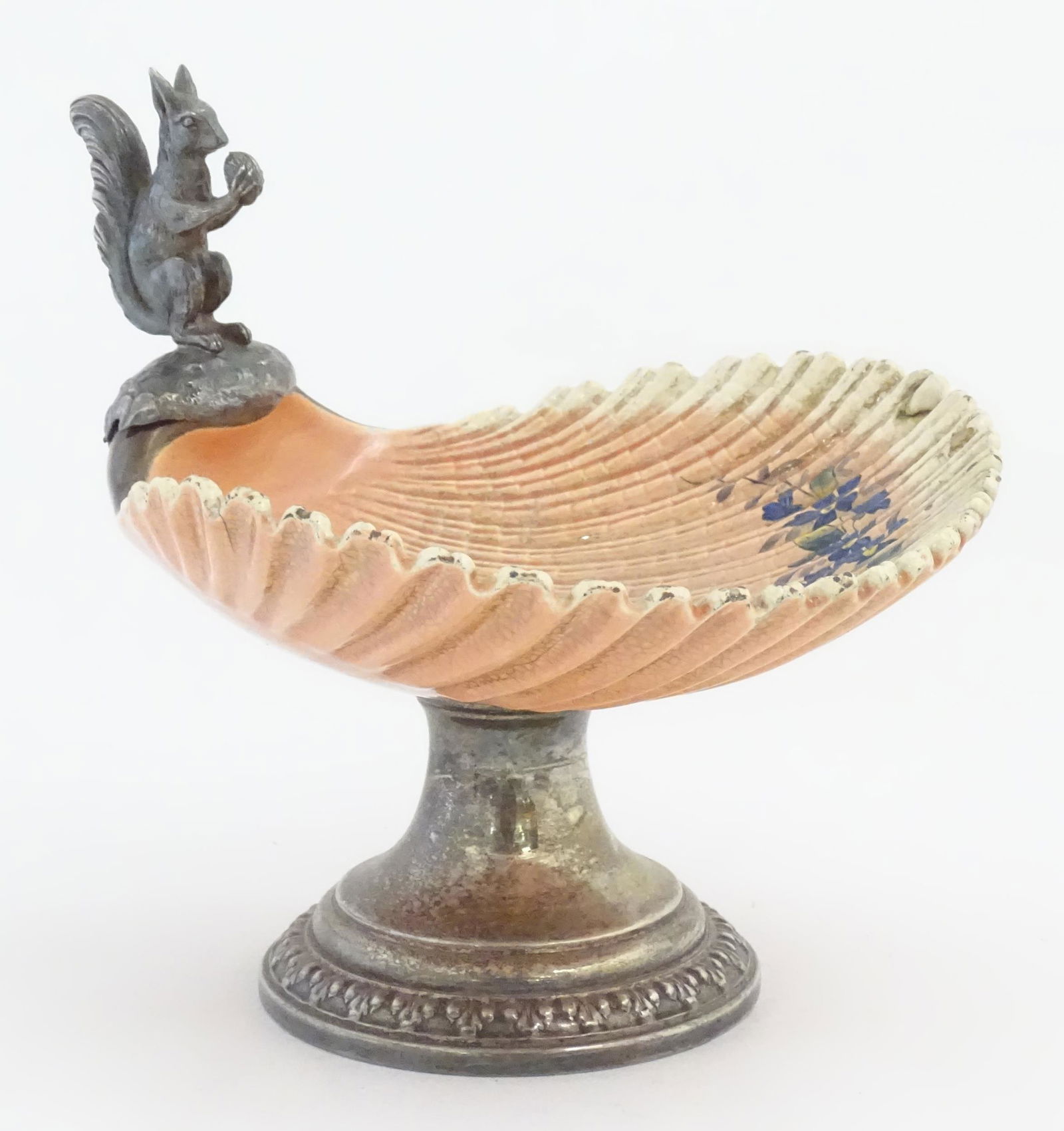 A Sarreguemines tazza / comport of shell form with flower detail, with silver plate foot and a model: A Sarreguemines tazza / comport of shell form with flower detail, with silver plate foot and a model of a squirrel holding a nut. Marked under and numbered 1432. Approx. 10" high