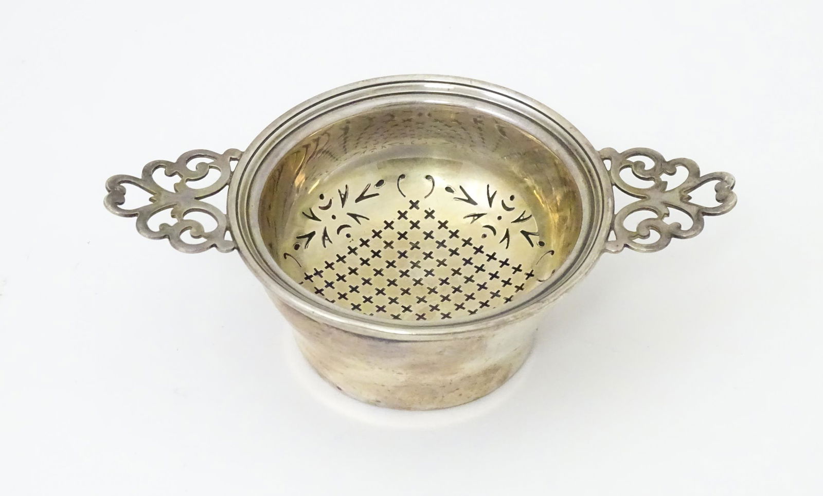A silver twin handled lemon / tea strainer with pierced detail and bowl under. Hallmarked Birmingham: A silver twin handled lemon / tea strainer with pierced detail and bowl under. Hallmarked Birmingham 1936 maker Adie Bros Ltd and stamped Greaves New St Birmingham. 5" wide overall.