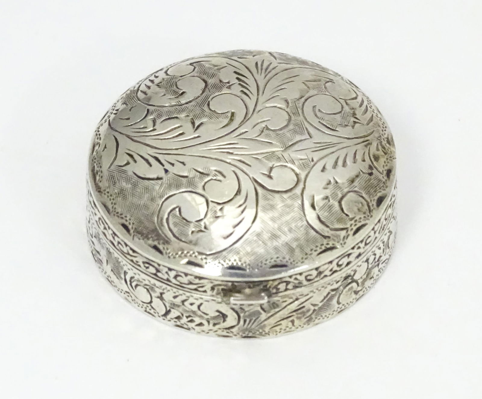 A .925 silver pill box of circular form with engraved acanthus scroll detail. Approx. 1 1/4": A .925 silver pill box of circular form with engraved acanthus scroll detail. Approx. 1 1/4" diameterPlease Note - we do not make reference to the condition of lots within descriptions. We are however