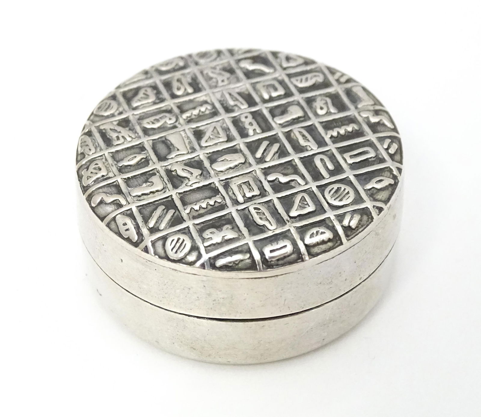 An Egyptian white metal pill box with hieroglyphics decoration to lid. Approx. 1 1/4" diameter: An Egyptian white metal pill box with hieroglyphics decoration to lid. Approx. 1 1/4" diameterPlease Note - we do not make reference to the condition of lots within descriptions. We are however happy