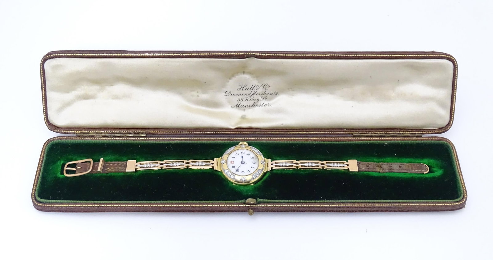 An 18ct gold cased ladies wristwatch set with 12 diamonds, with white enamel dial, and 15ct gold: An 18ct gold cased ladies wristwatch set with 12 diamonds, with white enamel dial, and 15ct gold bracelet strap with leather adjustment marked with patent no. 3680/0, the case bearing import marks for