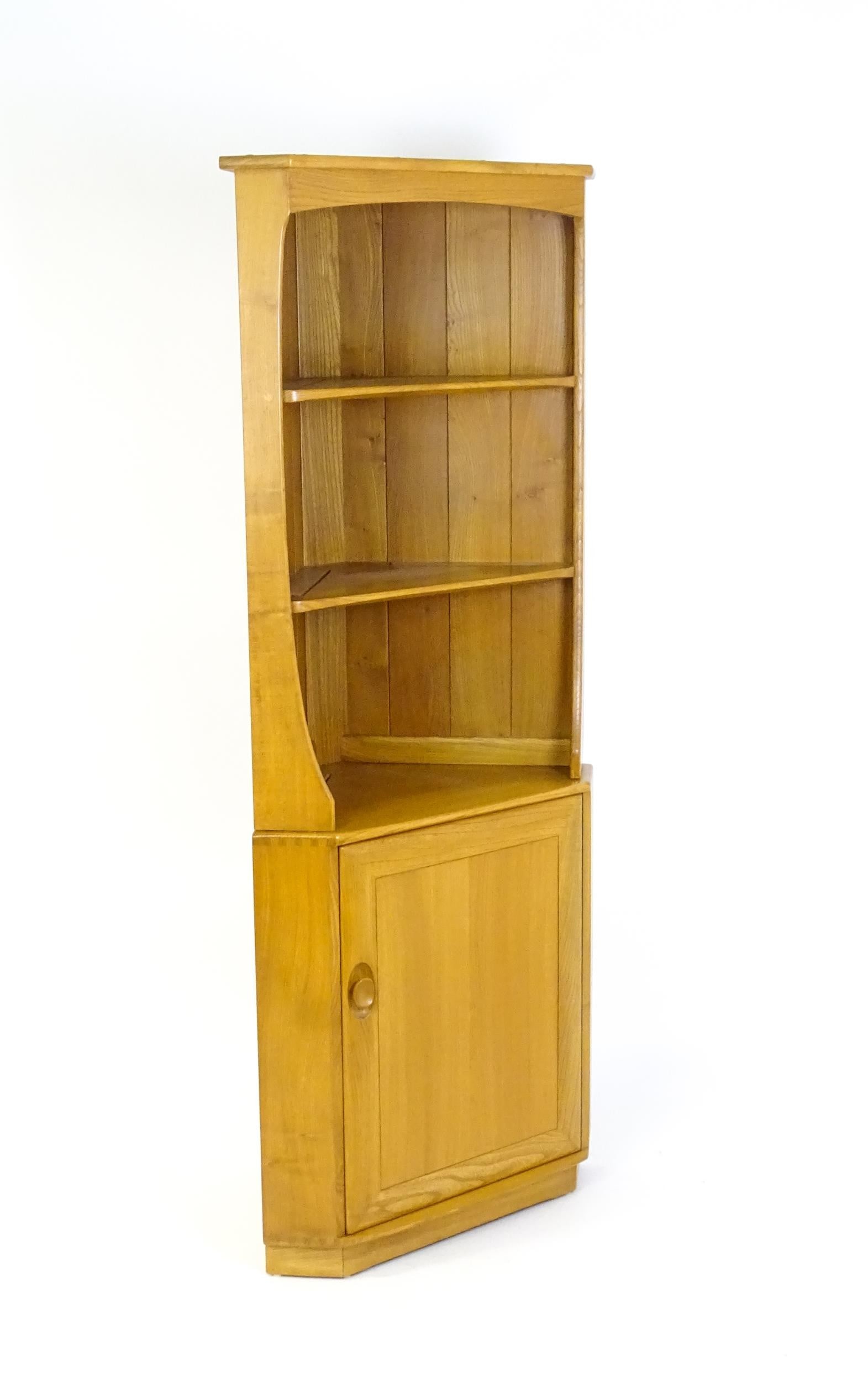 Vintage / Retro: An elm Ercol Windsor corner cabinet with a moulded cornice above three shelves and: Vintage / Retro: An elm Ercol Windsor corner cabinet with a moulded cornice above three shelves and a panelled base containing two shelves. 71" high.Please Note - we do not make reference to the condi