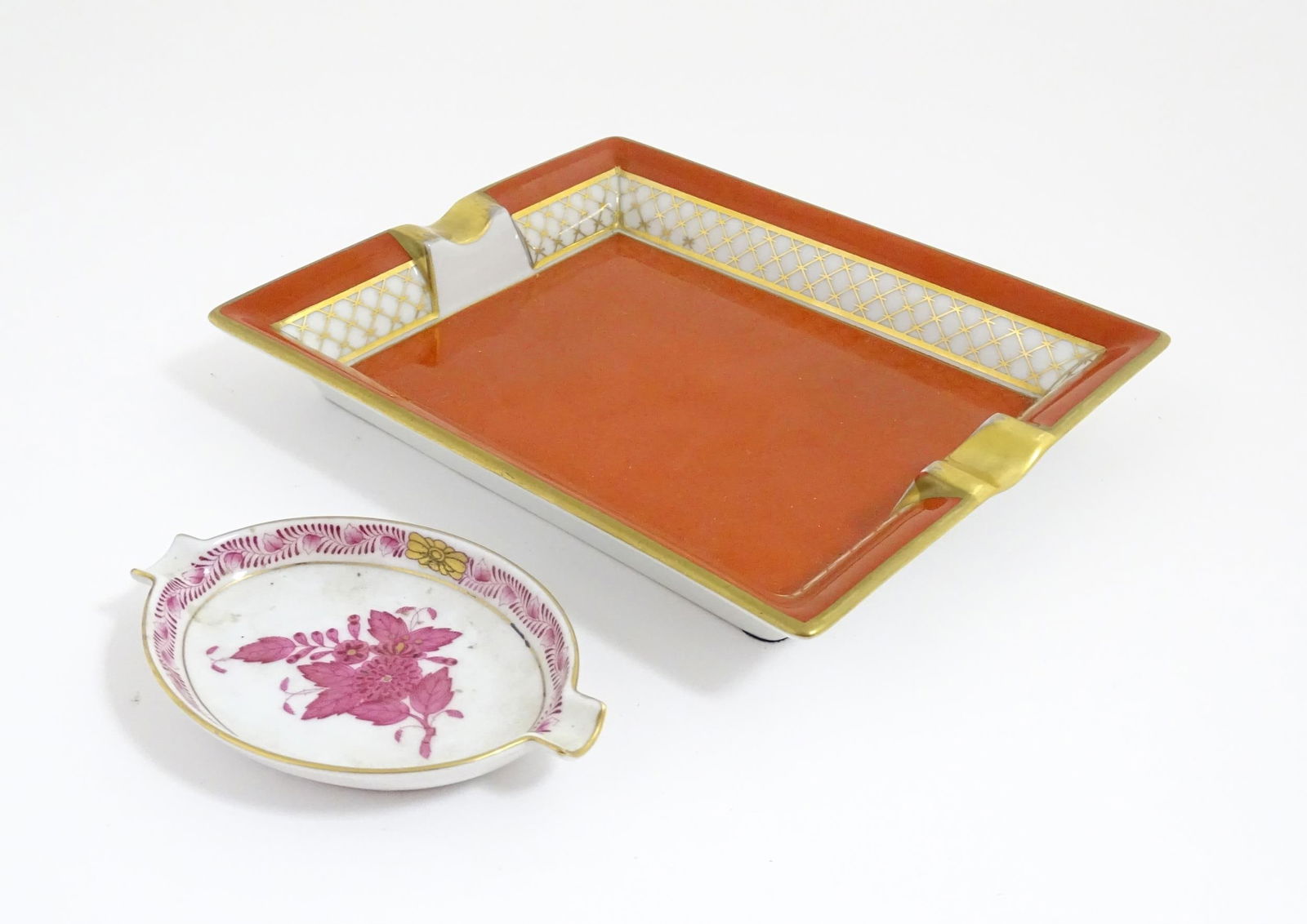 A Herend porcelain ashtray of oval form decorated in the Chinese Bouquet pattern in pink. Together: A Herend porcelain ashtray of oval form decorated in the Chinese Bouquet pattern in pink. Together with a Dubarry Limoges cigar ashtray of rectangular form with a red ground and gilt detail. Both mark