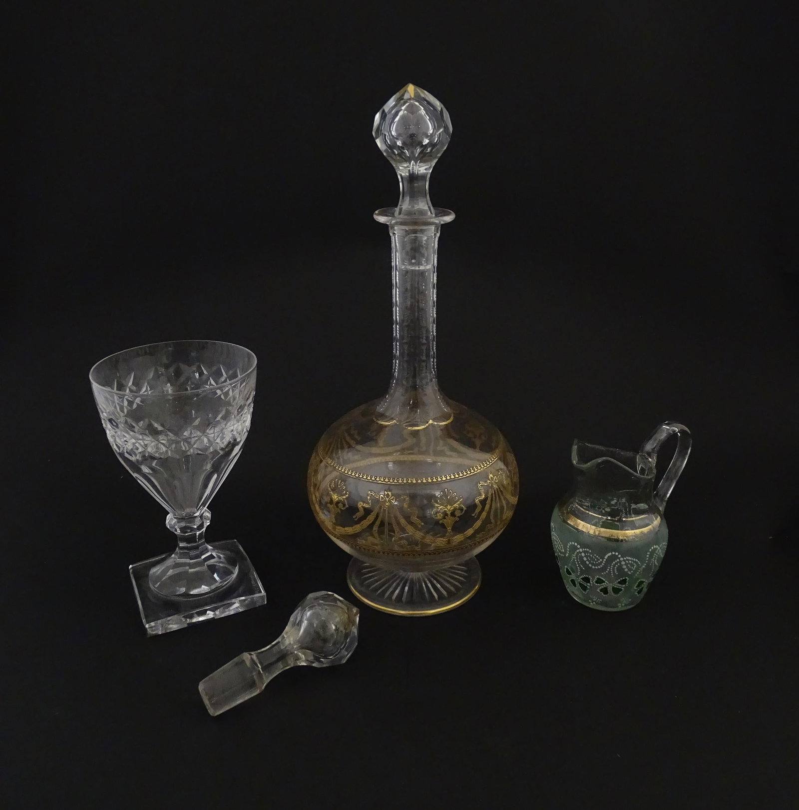 Three items of glassware comprising a Val Saint Lambert glass with squared foot, a decanter with: Three items of glassware comprising a Val Saint Lambert glass with squared foot, a decanter with gilt detail and an additional stopper, and a small glass jug with shamrock detail. Decanter approx. 12"