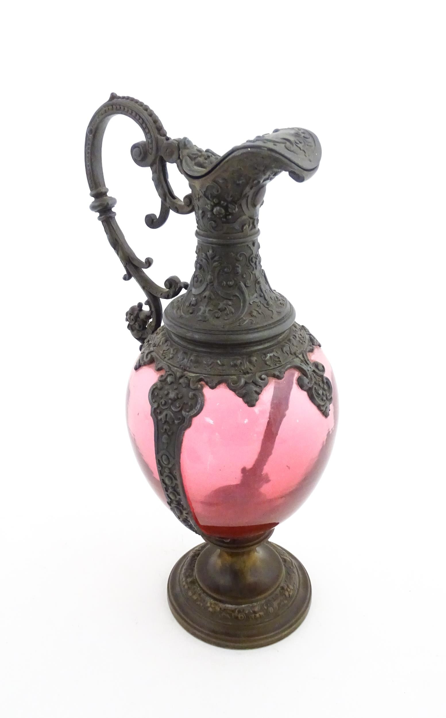 A Victorian cranberry glass claret jug with decorative metal mounts and handle. Approx. 13" high: A Victorian cranberry glass claret jug with decorative metal mounts and handle. Approx. 13" high Please Note - we do not make reference to the condition of lots within descriptions. We are however hap