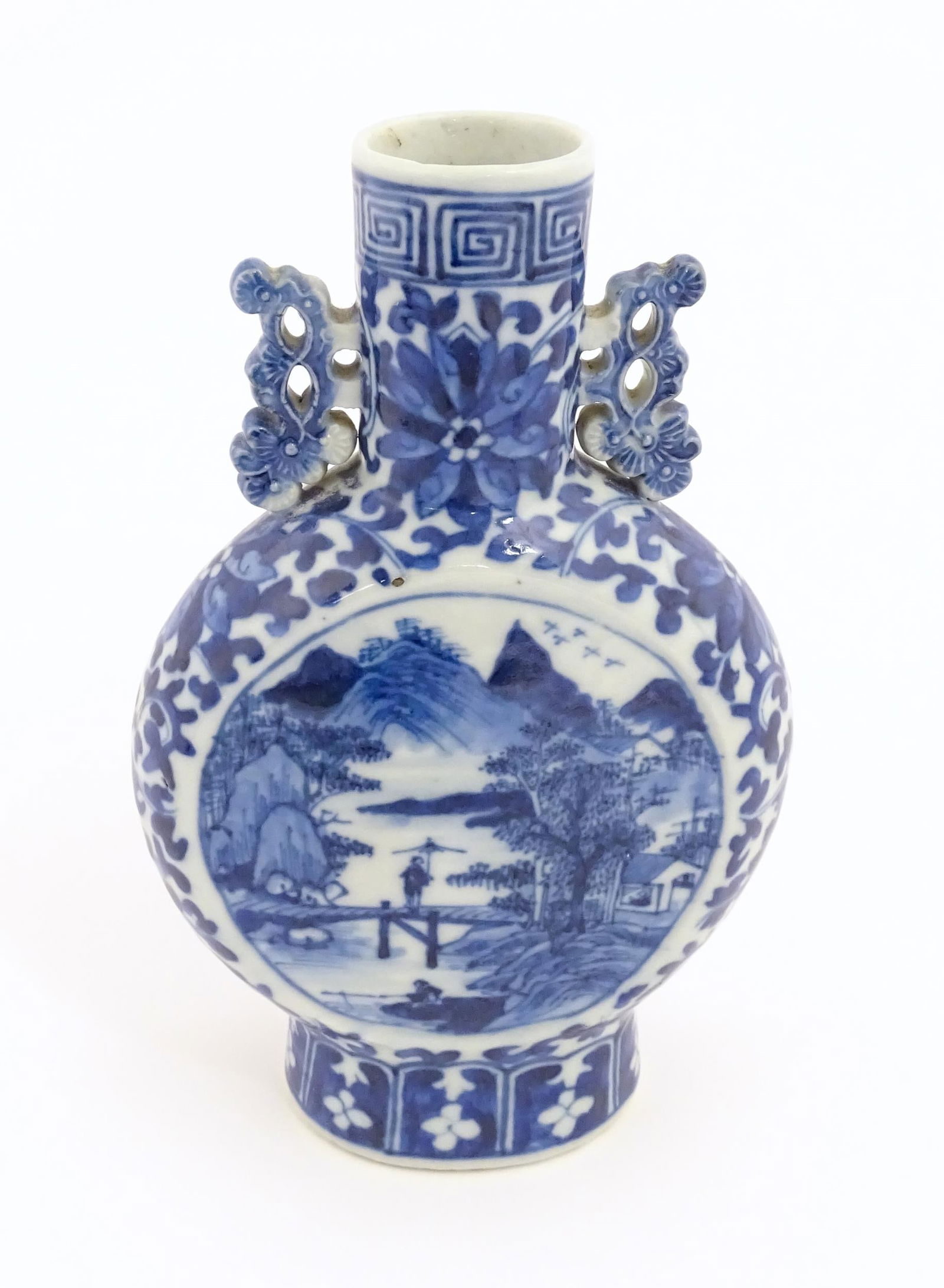A Chinese blue and white moon flask vase with twin foliate handles, decorated with central vignettes: A Chinese blue and white moon flask vase with twin foliate handles, decorated with central vignettes depicting landscape scenes with a figure on a bridge, bordered by scrolling floral and foliate deta