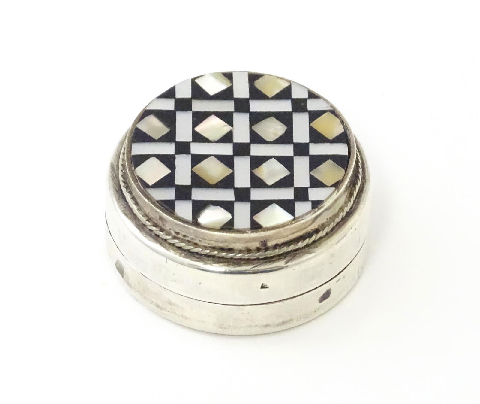 An Egyptian silver pill box set with onyx and mother of pearl detail. Approx. 1 3/8" diameter: An Egyptian silver pill box set with onyx and mother of pearl detail. Approx. 1 3/8" diameter Please Note - we do not make reference to the condition of lots within descriptions. We are however happy