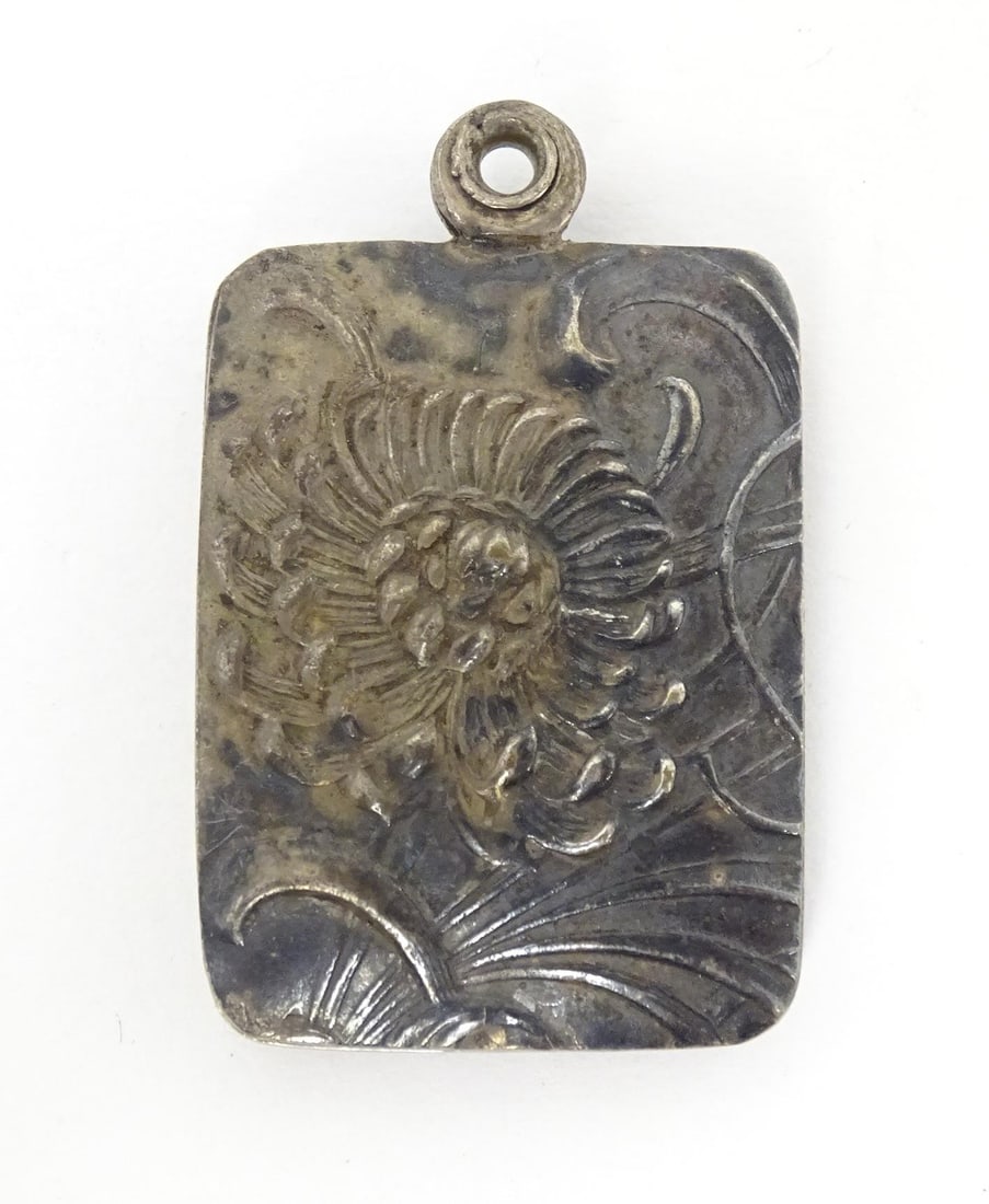 A white metal pendant locket of oblong form with chrysanthemum floral decoration and opening to: A white metal pendant locket of oblong form with chrysanthemum floral decoration and opening to reveal a mirror within. Approx 1 1/2" longPlease Note - we do not make reference to the condition of lot