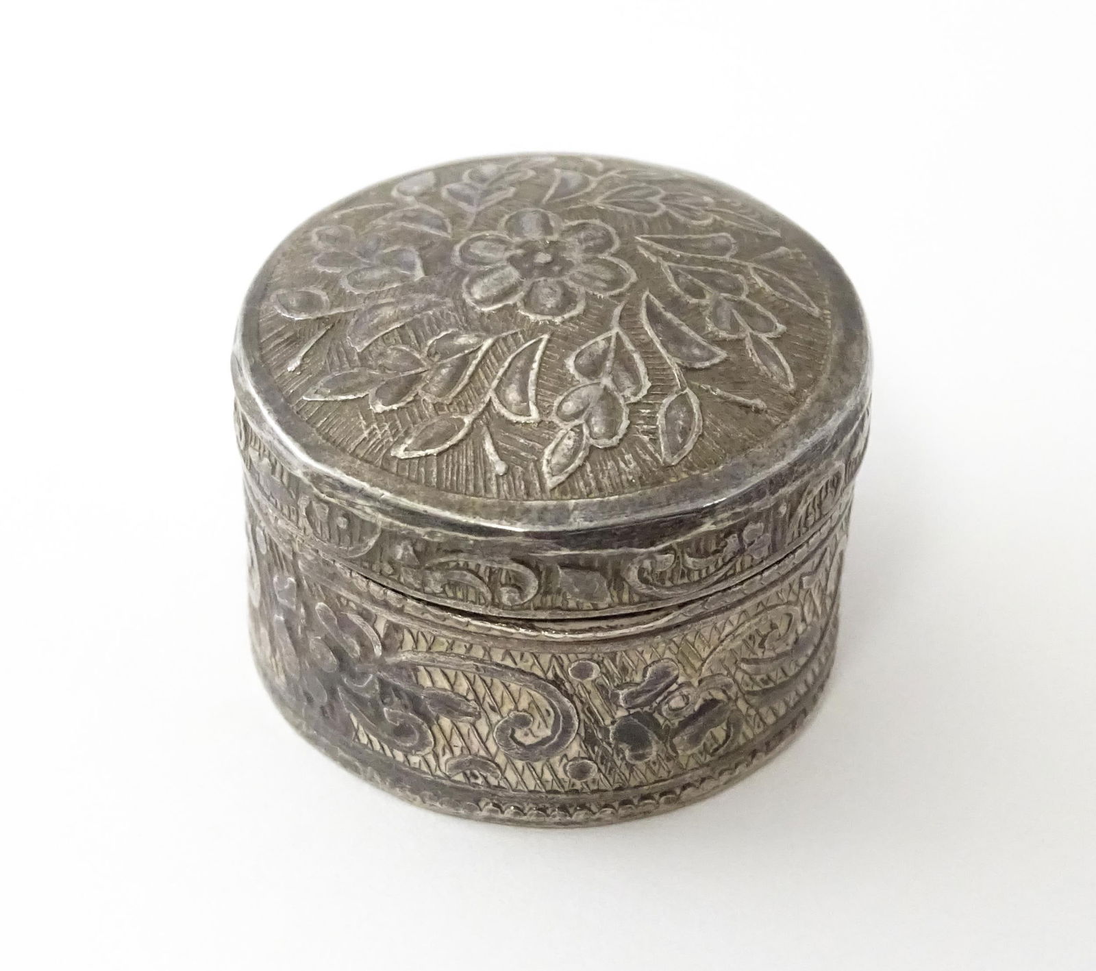 A white metal pill box with floral and foliate decoration. Approx. 1 1/4" diameter: A white metal pill box with floral and foliate decoration. Approx. 1 1/4" diameterPlease Note - we do not make reference to the condition of lots within descriptions. We are however happy to provide a