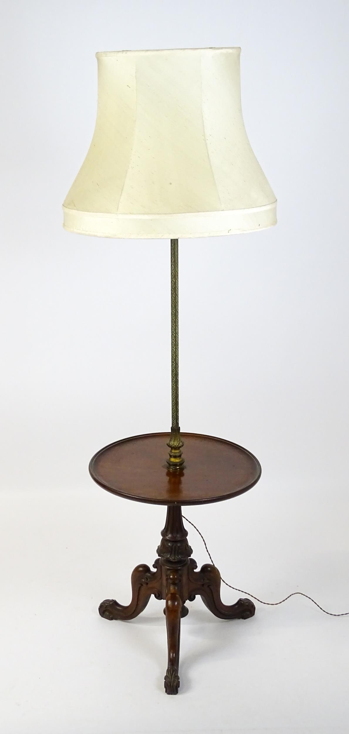 An Edwardian mahogany standard lamp with a brass column and dished circular shelf raised on three: An Edwardian mahogany standard lamp with a brass column and dished circular shelf raised on three carved cabriole legs. 58" high.Please Note - we do not make reference to the condition of lots within