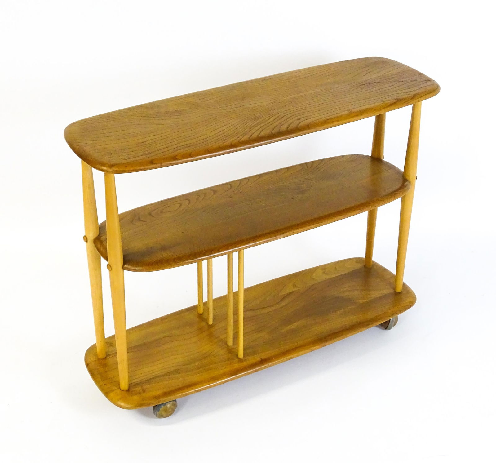 Vintage / Retro: An Ercol elm trolley with three shaped tiers on four turned supports and raised on: Vintage / Retro: An Ercol elm trolley with three shaped tiers on four turned supports and raised on ball castors. 36" wide x 13" deep x 28" high.Please Note - we do not make reference to the condition