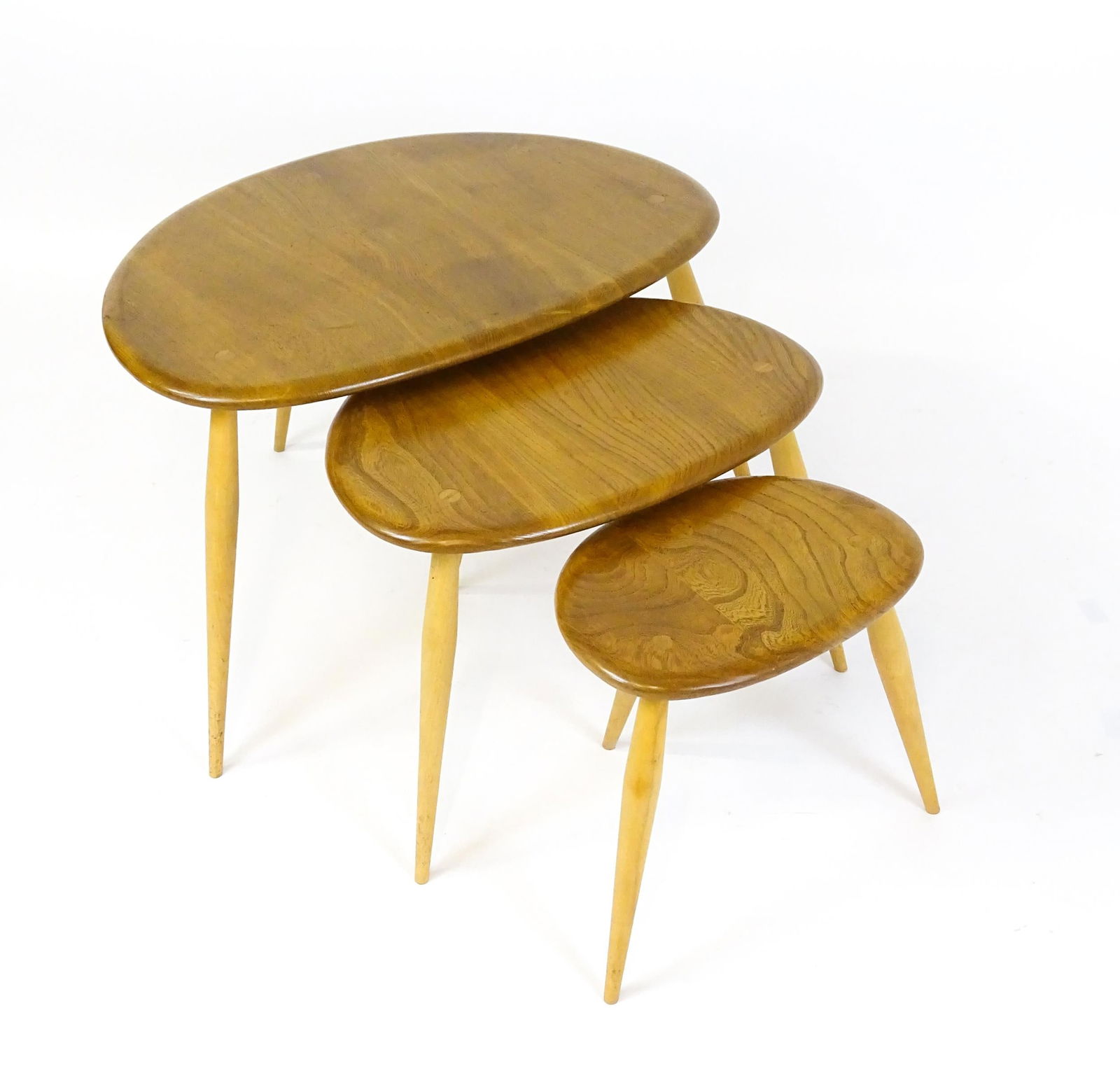 An Ercol nest of three elm pebble tables raised on turned tapering legs. 26" wide x 17" deep x 16": An Ercol nest of three elm pebble tables raised on turned tapering legs. 26" wide x 17" deep x 16" high.Please Note - we do not make reference to the condition of lots within descriptions. We are howe
