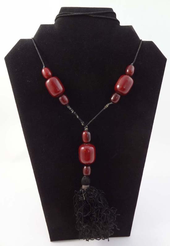 A black cord long necklace set with cherry amber / bake: A black cord long necklace set with cherry amber / bakelite beads terminating in a tassel. The whole approx 40" long