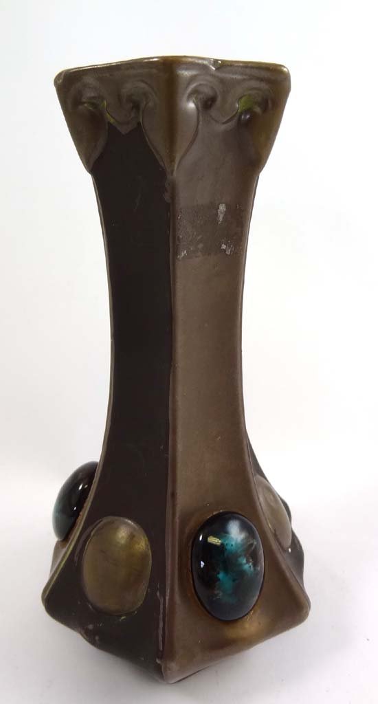 A Bretby Arts & Crafts Bronze and jewelled ware vase of: A Bretby Arts & Crafts Bronze and jewelled ware vase of slightly waisted hexagonal shape, modelled in red clay glazed and finished to resemble bronze and the base set with ceramic Ruskin like cabochon