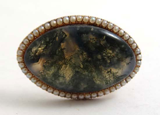 A gilt metal brooch of oval form set with moss agate ca: A gilt metal brooch of oval form set with moss agate cabachon bordered by seed pearls 1 1/4" wide