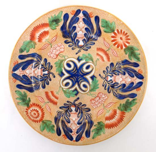 An early 19thC creamware plate decorated in Imari palet: An early 19thC creamware plate decorated in Imari palette with green detail with radiating design of stylised flowers and leaves on a white dotted iron red ground. Unmarked. Diameter 9"