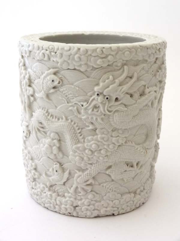 An Oriental late 19th/ early 20thC blanc de Chine pot,: An Oriental late 19th/ early 20thC blanc de Chine pot, modelled in high relief with mythological dragons and koi carp amongst scrolling waves. Indistinct marks to underside, signed by Wang Bing Rong Z