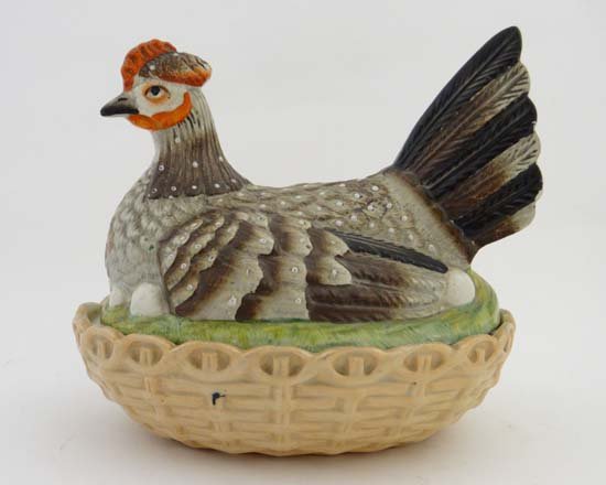 A Victorian Staffordshire hen on nest, the hen: A Victorian Staffordshire hen on nest, the hen decorated in brown, beige and black with iron red and white detail, sits on eggs on a green grassy ground above a beige basket weave base. Length 8"