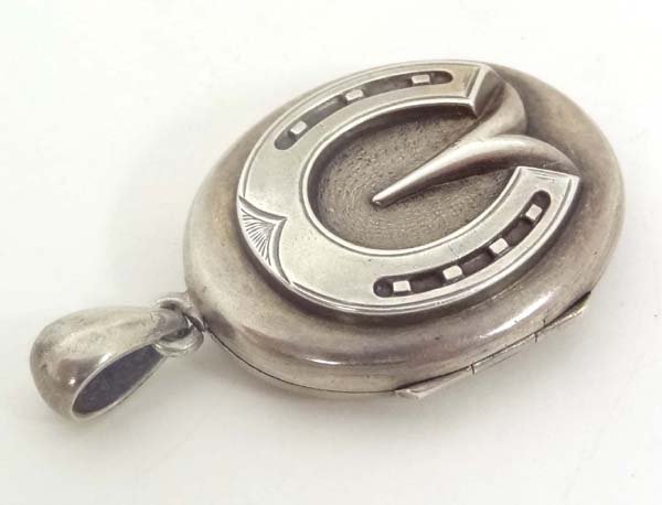 A white metal locket set with horse hoof and shoe: A white metal locket set with horse hoof and shoe decoration to one side and engraved decoration to other 1 1/2" high £80 - 120