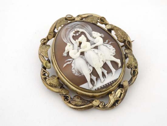 A late 19thC / early 120thC cameo brooch the central: A late 19thC / early 120thC cameo brooch the central cameo section depicting the 3 graces to one side and revolving to reveal glazed locket section within an ornate gilt metal foliate surround 2 3/4" 