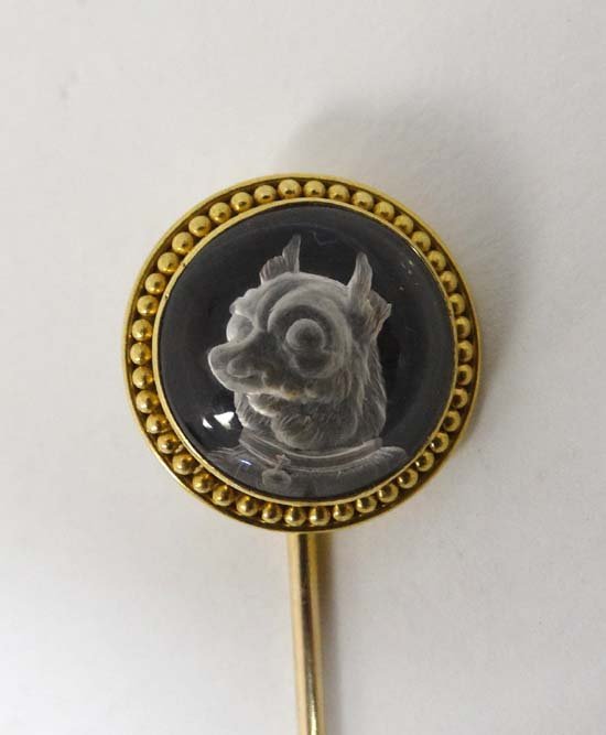 A 19thC gilt metal stick pin surmounted by Essex: A 19thC gilt metal stick pin surmounted by Essex Crystal reverse glass intaglio depicting the head of a terrier dog Please Note - we do not make reference to the condition of lots within catalogue des