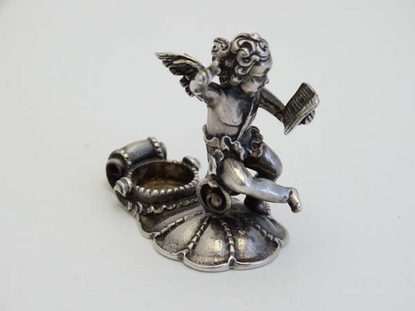 A silver small model of a cherub upon a scallop shell: A silver small model of a cherub upon a scallop shell base 1 3/4" high Please Note - we do not make reference to the condition of lots within catalogue descriptions. We are however happy to provide ad