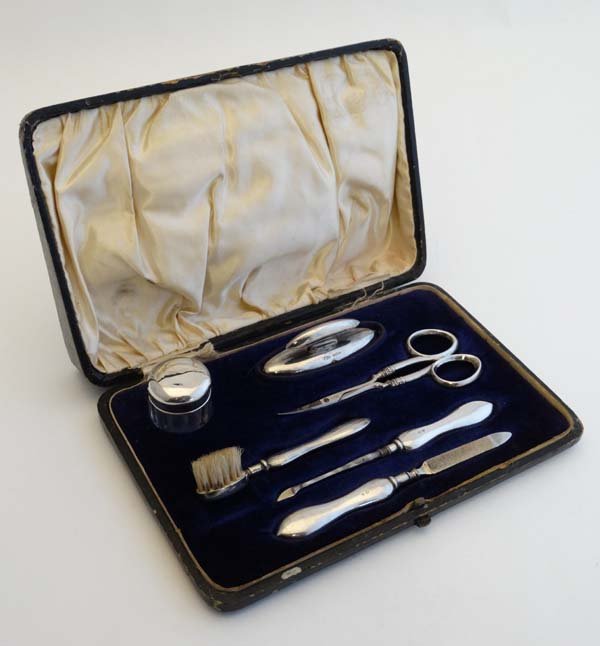 A cased silver mounted manicure set comprising nail: A cased silver mounted manicure set comprising nail buffer, nail file, scissors, pot, nail brush etc. Hallmarked Birmingham 1912 maker Adie Bros Ltd. Please Note - we do not make reference to the cond