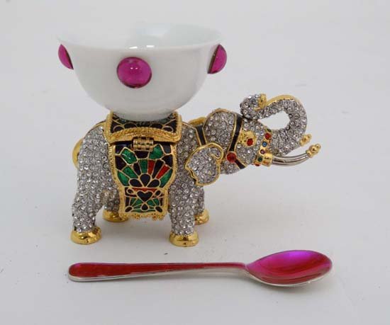 A 21stC enamelled and be-jwelled table salt in the form: A 21stC enamelled and be-jwelled table salt in the form of a dish atop an elephant with an enamelled spoon. The whole standing 3" high Please Note - we do not make reference to the condition of lots w
