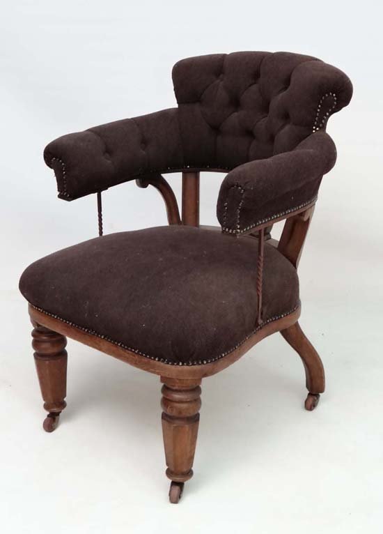 A 19thC oak button back open arm office chair ( in a: A 19thC oak button back open arm office chair ( in a cock fighting style) with over stuffed seat and tapering octagonal front legs with castors. 34 1/2" high
