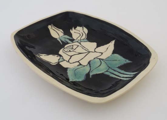 A rectangular Leaper Newlyn studio pottery dish,: A rectangular Leaper Newlyn studio pottery dish, decorated with cream roses on a black ground and cream border, bears impressed signature verso. 10 1/2'' long x 8'' wide.