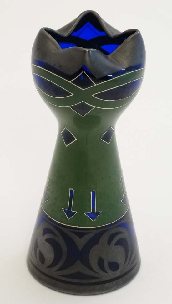 Modernist movement, manner of Peter Behrens 1869 - 1940: Modernist movement, manner of Peter Behrens 1869 - 1940 German. A pewter and white lined green enamel decorated blue glass vase, with pinched top, 7 1/8'' high.
