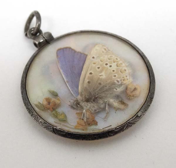 A double sidled glazed pendant locket with white metal: A double sidled glazed pendant locket with white metal mounts and mother of pearl centre with pressed flowers and butterfly decoration. Approx 1'' diameter