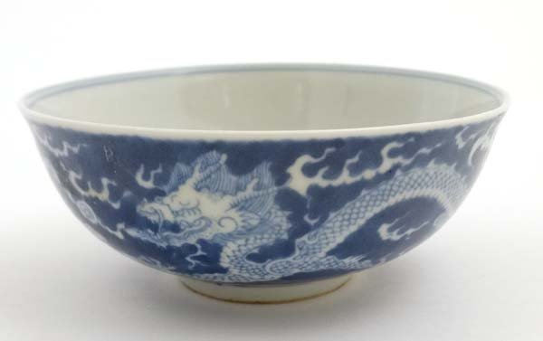 A Chinese blue and white dragon bowl decorated with 5: A Chinese blue and white dragon bowl decorated with 5 clawed dragons and flaming pearls of wisdom amongst scrolling clouds, having blue Chinese 6 character mark to base. 6'' diameter.