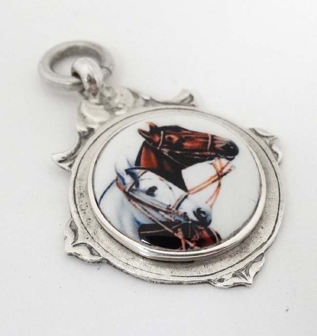 A hallmarked silver fob with later applied ceramic: A hallmarked silver fob with later applied ceramic cabochon depicting two horse heads 1 1/2'' long