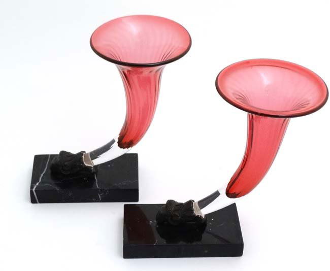 A pair of of cranberry glass epergnes, the glass flutes: A pair of of cranberry glass epergnes, the glass flutes supported by rams heads mounted upon marble bases. Approx 9 1/2'' high