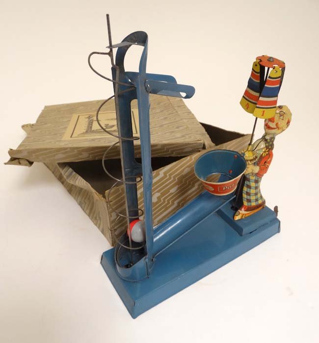 A Dely, Germany clockwork tinplate ''Pot-Ball' toy,: A Dely, Germany clockwork tinplate ''Pot-Ball' toy, marked D.R.G.M, formed as a clown with umbrella, the balls falling into a pot, in original box, marked to pot. 9 1/2'' high.