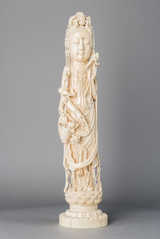 Large Ivory Carved Figure of GuanYin, 19th Century,: 19 of tusk-form and standed on lotus, dressed in sweeping robes with long beaded necklace, and a freshwater pearl on the forehead, while holding a basket of flowers in one hand, and a fly whisk in the