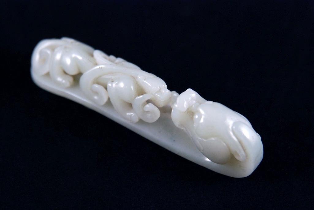 A CHINESE WHITE JADE BELT HOOK: Of white jade with a reticulated jaw to the draon-head hook facing a deeply undercut chilong string on the curving handle reversed by an oval button, matrix presenting a very pale gray-green tinge, 18