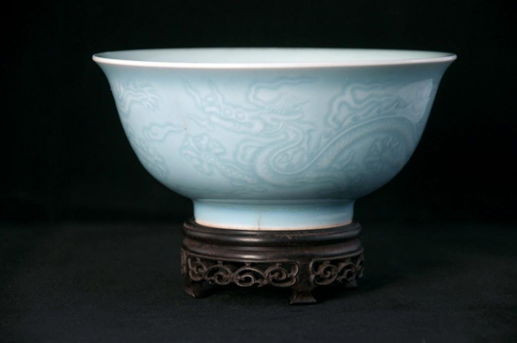 A BLUE GLAZED BOWL WITH CARVED DRAGON MOTIF: Deep bowl with decoration of two dragon motif alternating with amidst flames of clouds, inverted bell form with a flared rim, Six character Qianlong mark. Height: 2 7/8in (7cm), Diameter: 6in (15cm).