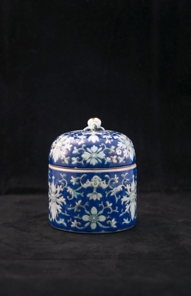 ENAMELED BLUE CYLINDRICAL COVERED BOX: a deep blue with domed lid centering a parcel-gilt molded peach form finial and enameled throughout with blossoms and stylized bats reversing to an underside with an overglaze iron-red square characte