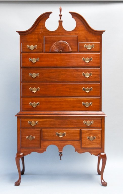 A cherry chest on stand.: By Pennsylvania House, with a broken scroll pediment with urn finial, over three over four drawers, the top center fan carved, on a lowboy base with one over three drawers, a scalloped apron with pend
