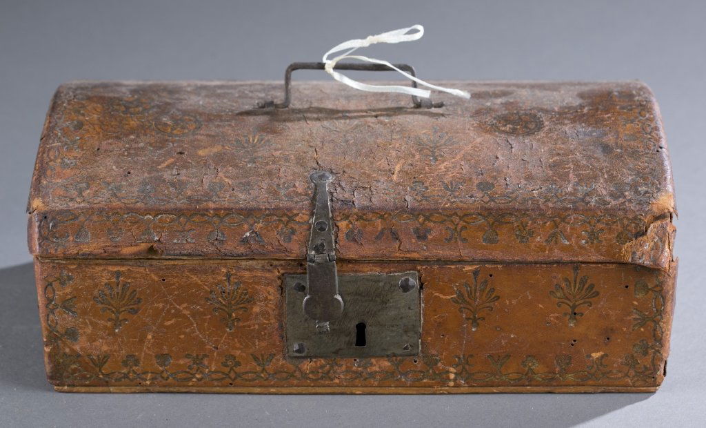 Tooled Leather Carrying Case: One tooled leather box with iron latch and lock. Cracking to the leather, lined with floral book page. 4 1/2" H x 11" L x 6" D Provenance: The Estate of Robert V. Hatcher, Jr. of Manakin-Sabot, VA.