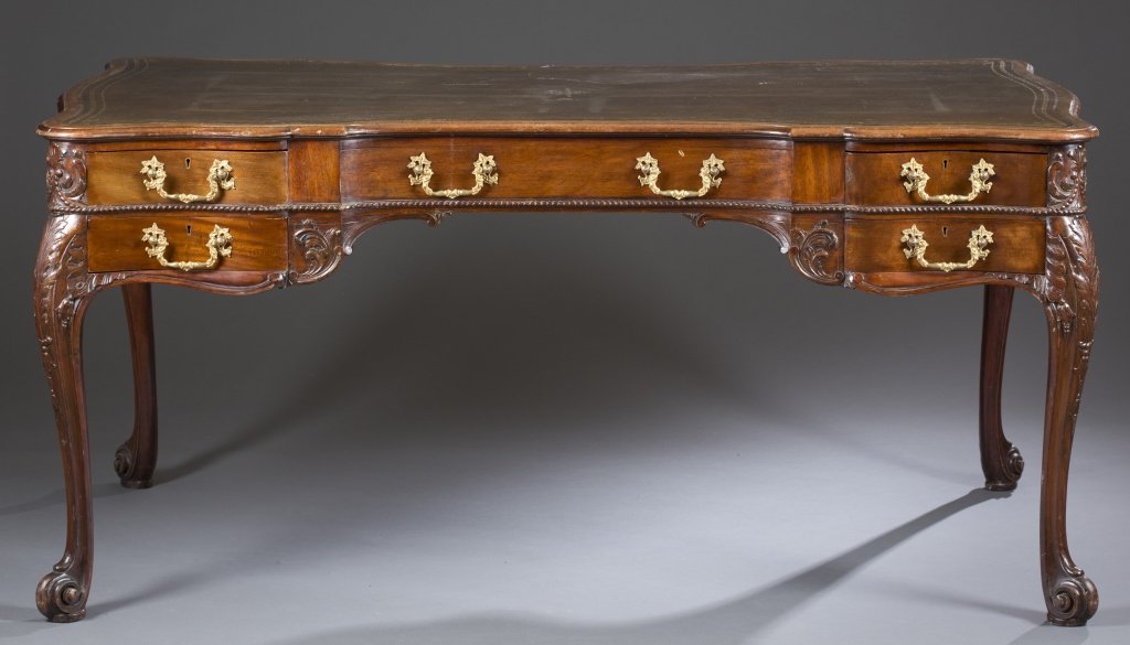 Early 20th c. English Chippendale Partners' Desk: Walnut with mahogany secondary. Leather inset top with wreath and leaf gilt inlay around the rim. Comprised of nine drawers with one faux drawer. Retains red wash on drawers. Ornate Rococo-style brass