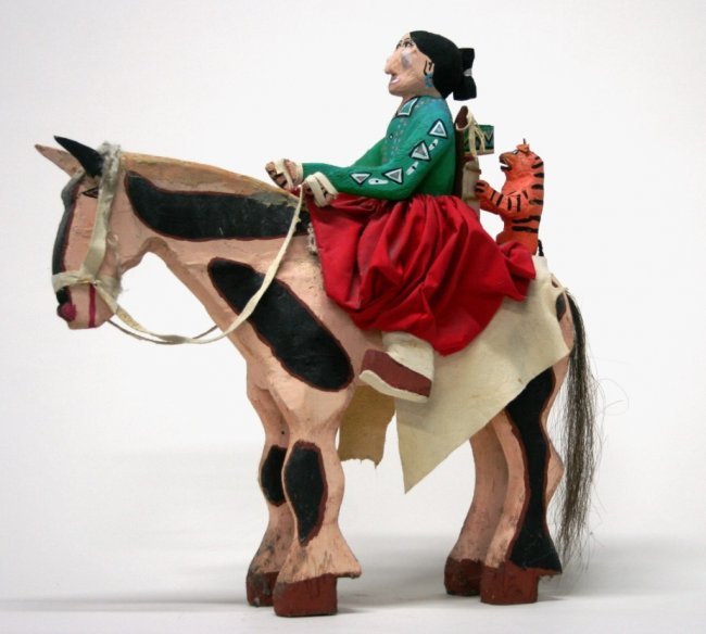 Delbert Buck (New Mexico/Navajo, b. 1946) Sculpture.: "Woman on Horse with Cradleboard and Orange Cat". Carved and polychrome painted wood sculpture depicting a woman with a baby and cat riding horseback. No signature or marks located. 23"h x 22 1/2"l x 