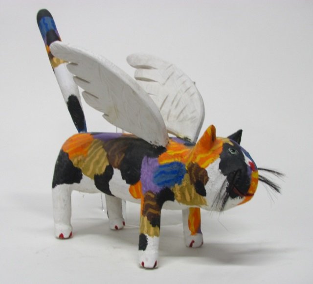 Miguel Rodriguez Carved Wooden Cat Sculpture.: Angel Cat.1999. New Mexican folk art carved wooden and polychrome painted cat with angel wings. On bottom, signed and dated. 18"h x 18 1/2"l x 9"w. Old repairs to both of the wings close to the body o