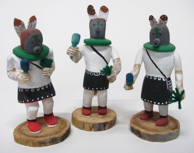 Johnson Antonio (Navajo Nation, NM., b. 1931).: "Corn Dancers". 1993. Group of three polychrome painted carved wood corn dancers with yarn details and deer pelt tails. On bottom, signed and dated. Tallest: 8 1/2"h.