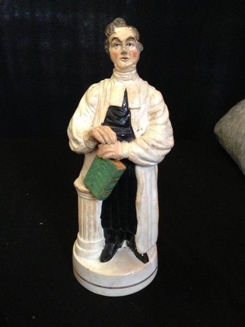 A 19th Century Staffordshire Figure of John Wesley: modelled in full robes, standing bible in hand resting against a classical pillar , and a socle base, h 24cm