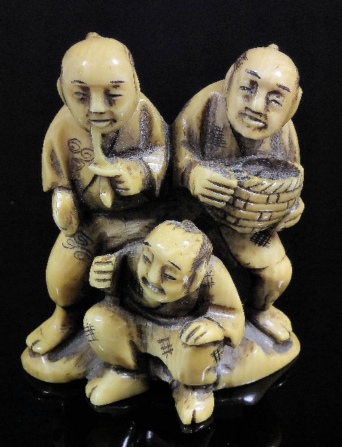 A Japanese ivory netsuke carved in the form of a g: A Japanese ivory netsuke carved in the form of a group of three figures, 2ins (52mm) high (Meiji period - character mark to base)