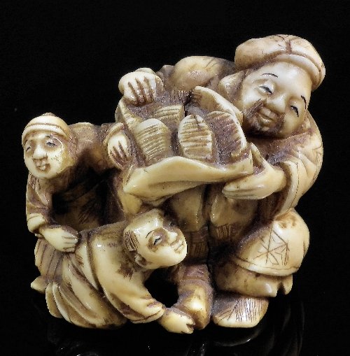 A Japanese ivory netsuke carved in the form of sho: A Japanese ivory netsuke carved in the form of shoe peddlar and two children, 1.5in (39mm) high (Meiji period)