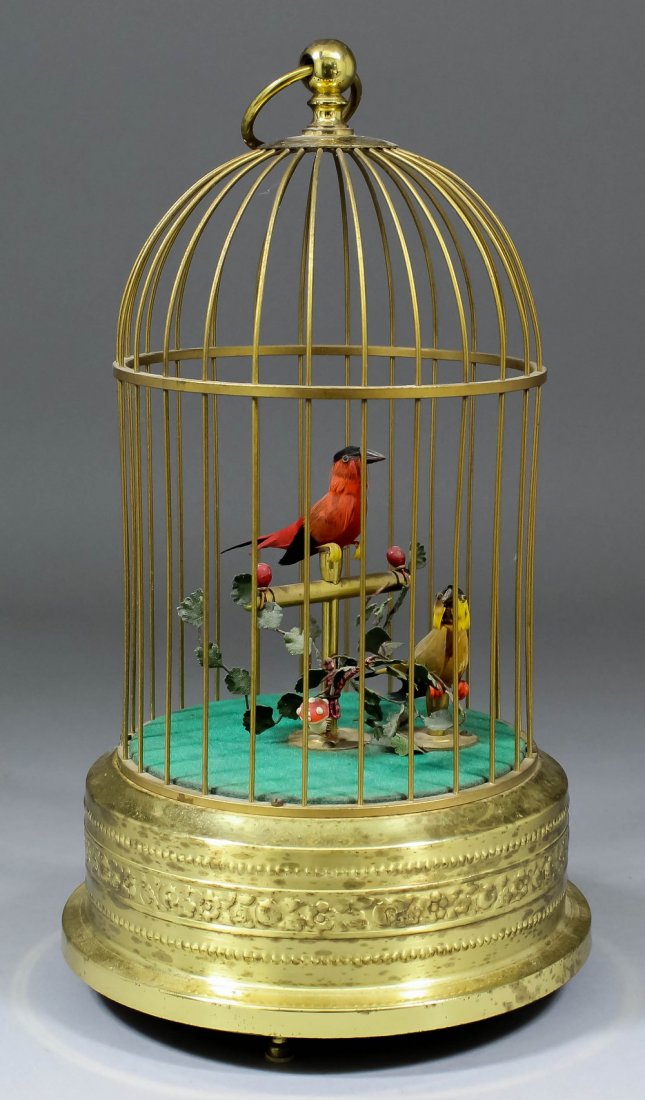 A mid 20th Century German "Bird In a Gilded Cage" autom: A mid 20th Century German "Bird In a Gilded Cage" automaton, the cylindrical cage containing two feathered mechanical birds, one on a perch, with embossed cylindrical base, 11.25ins high